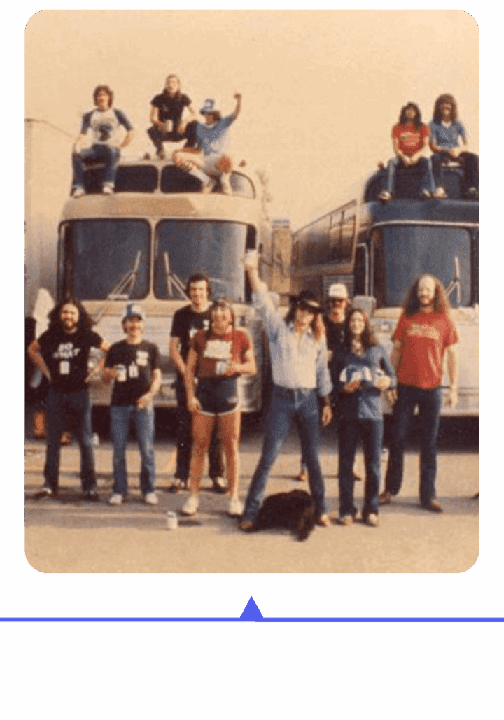 A group of people posing in front of two buses, some wearing matching shirts.