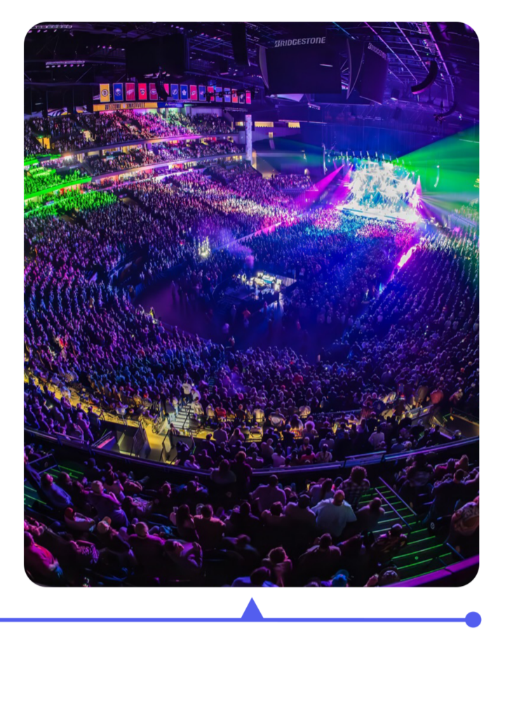A packed arena lit with colorful lights during a concert.